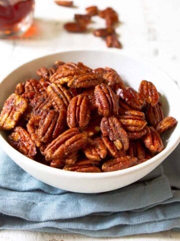 Maple pecans in a white bowl, sitting on a blue napkin.