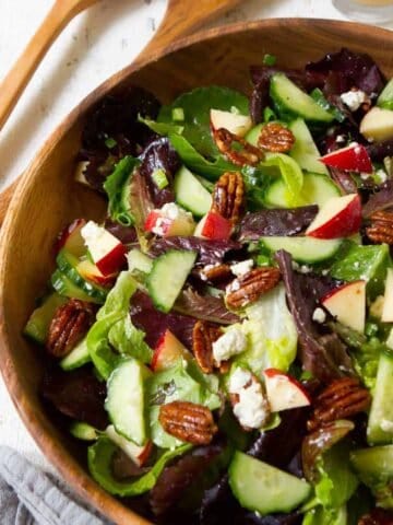 Wooden salad bowl filled with green salad with apples and pecans.