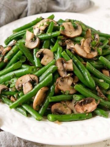 Sautéed green beans and mushrooms on a white plate, with a gray napkin.