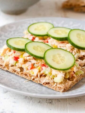 Tuna salad and cucumbers on crackers, on a gray plate.