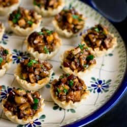 Hoisin mushroom mixture in mini phyllo cups on a blue flowered plate.