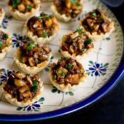 Hoisin mushroom mixture in mini phyllo cups on a blue flowered plate.