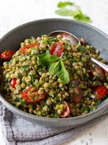 Lentil salad with tomatoes and herbs in a gray bowl.