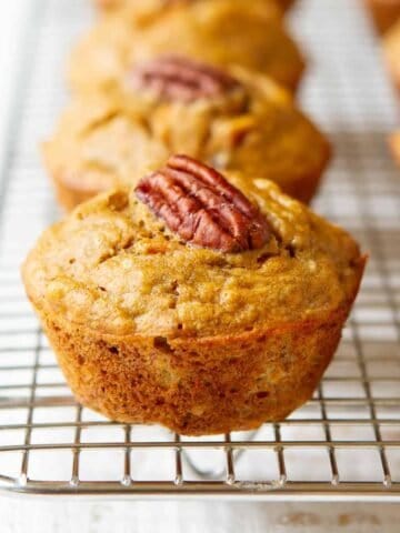 Banana carrot muffins, topped with pecan halves, on a wire rack.