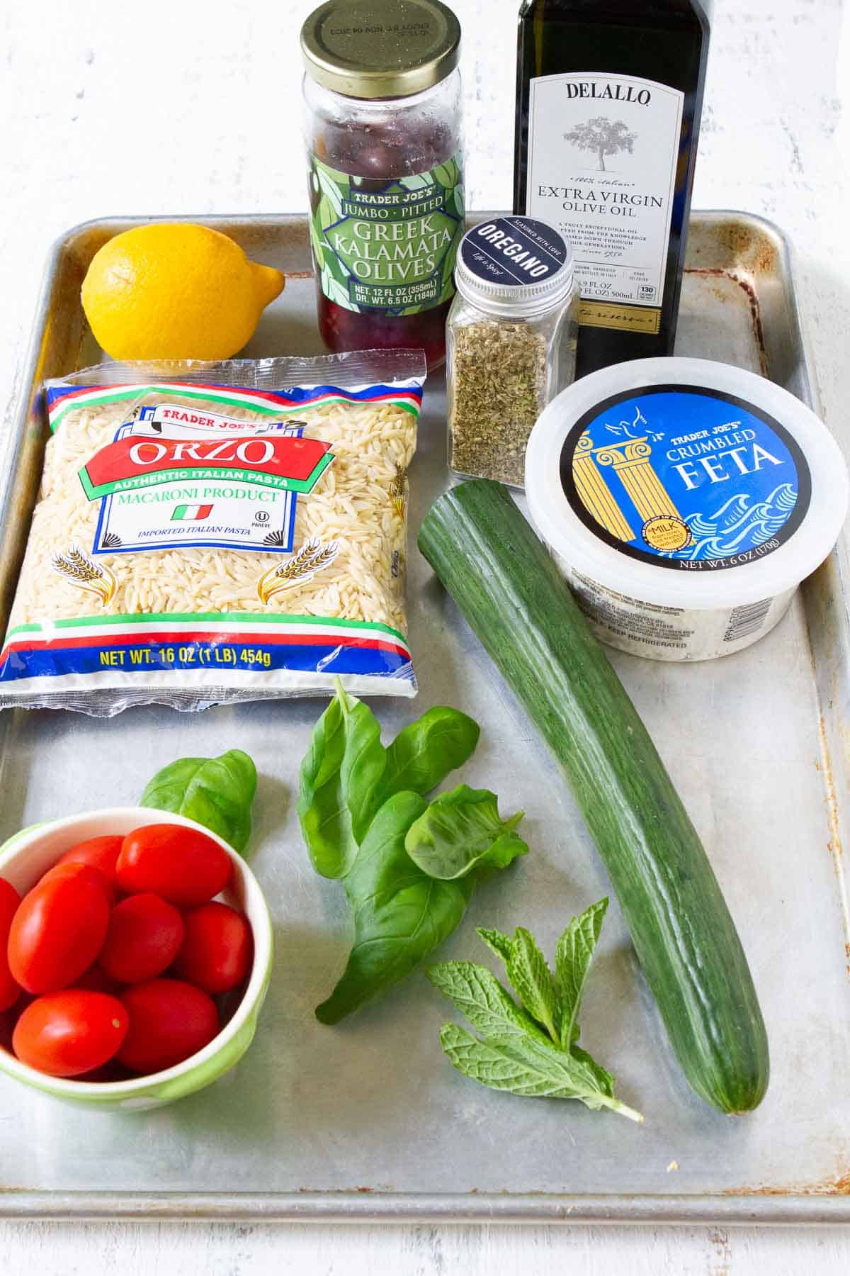 Package of orzo, tomatoes, cucumber, chickpeas, lemon and herbs on a baking sheet.