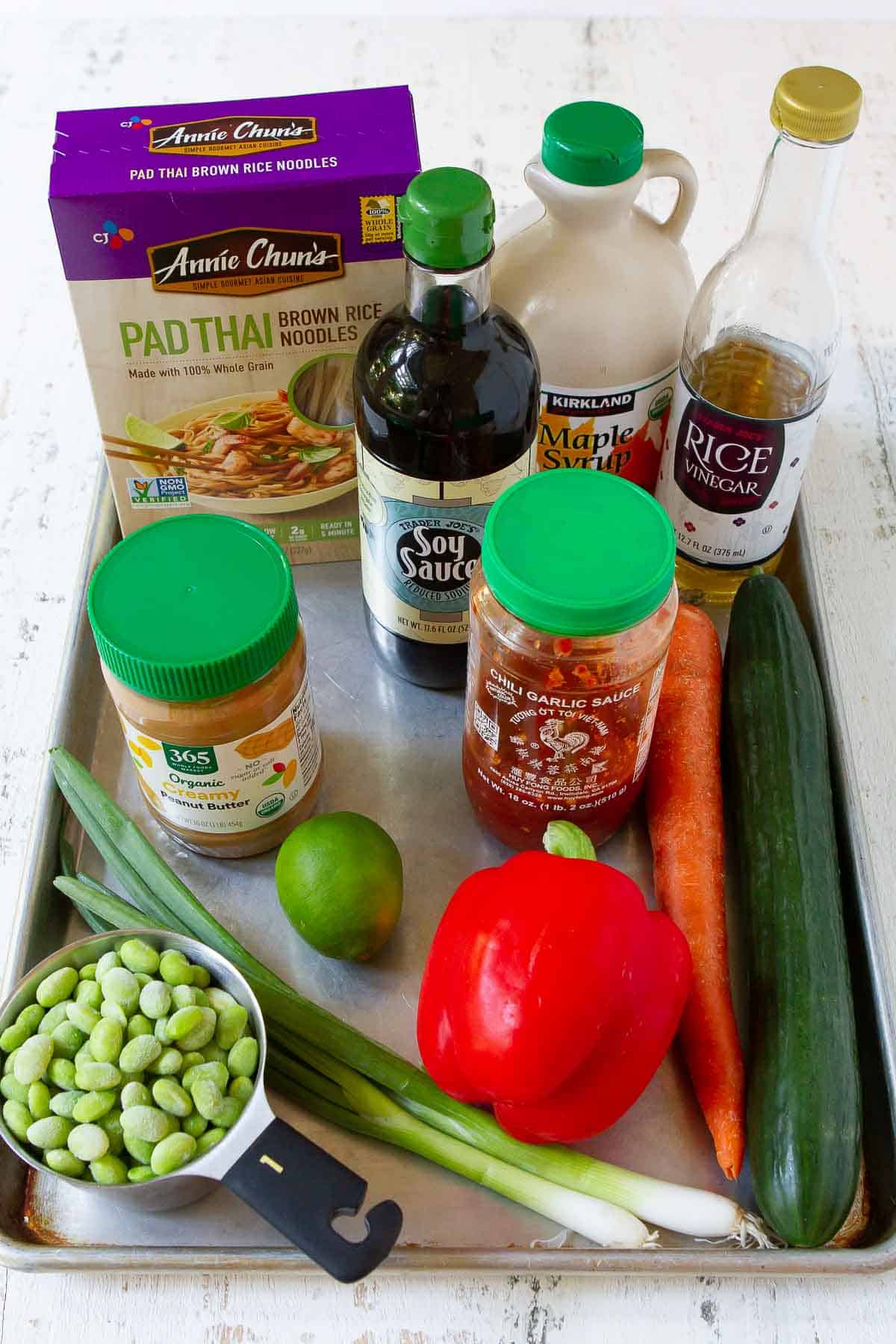 Rice noodles, edamame, vegetables, soy sauce, peanut butter and chili garlic sauce on a baking sheet.