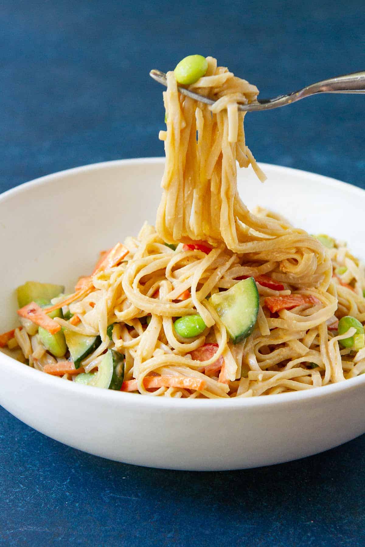 A fork scooping rice noodles out of a white bowl filled with noodles and vegetables.