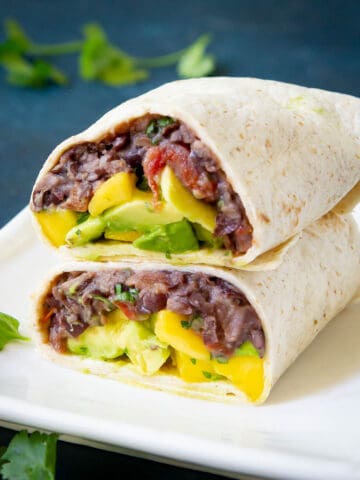 Black bean wraps filled with mango avocado salsa on a white plate.