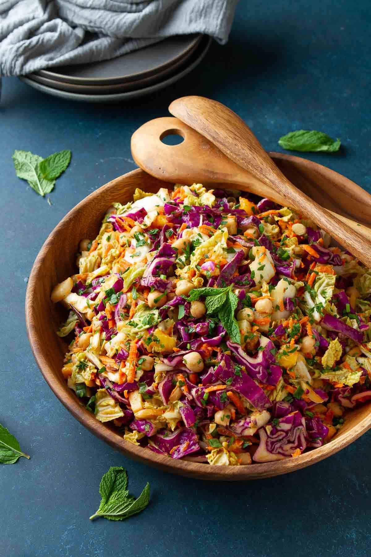 Wooden bowl filled with a Thai-inspired slaw. Gray plates and napkin on the side.