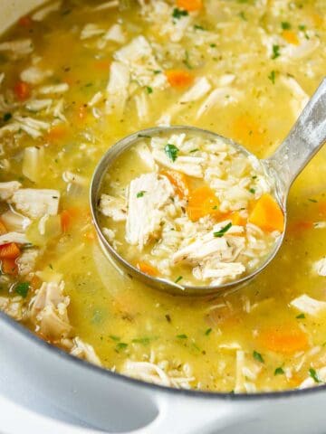 A ladle dipping into a white saucepan full of turkey rice soup.