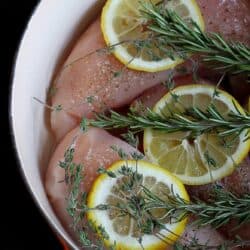 Raw chicken, lemon and rosemary sprigs in a large saucepan.