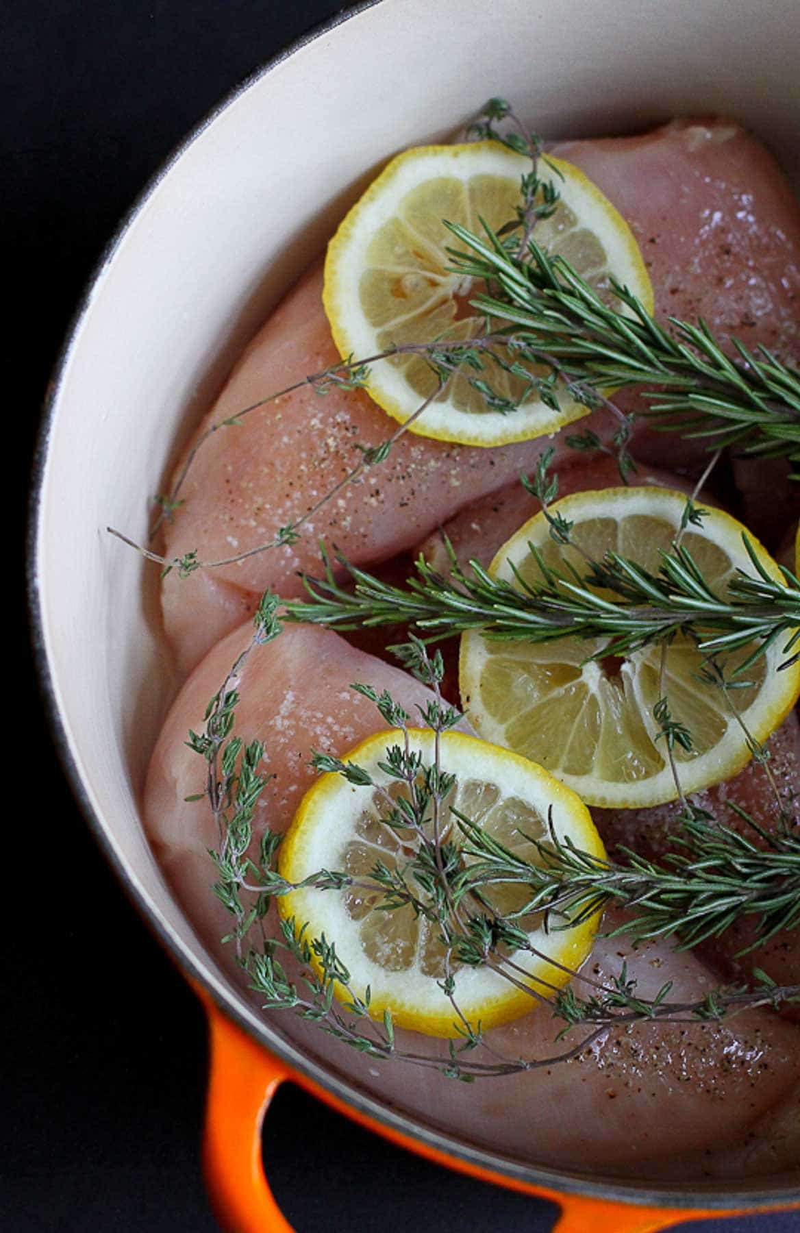 Raw chicken, lemon and rosemary sprigs in a large saucepan.