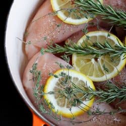 Lemon slices, rosemary sprigs and raw chicken in a saucepan.