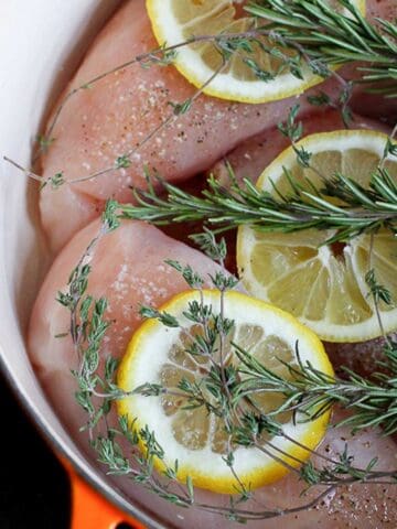 Lemon slices, rosemary sprigs and raw chicken in a saucepan.