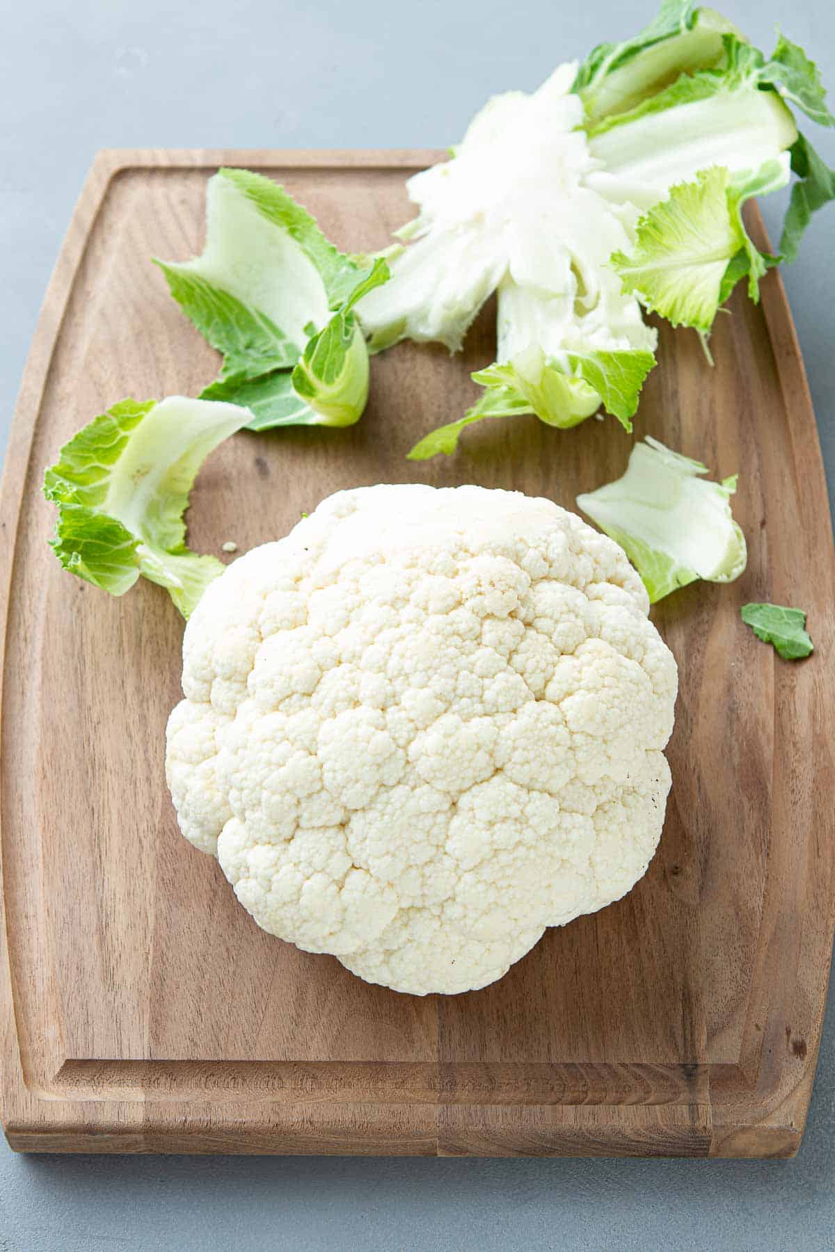 A head of cauliflower on a wooden cutting board.