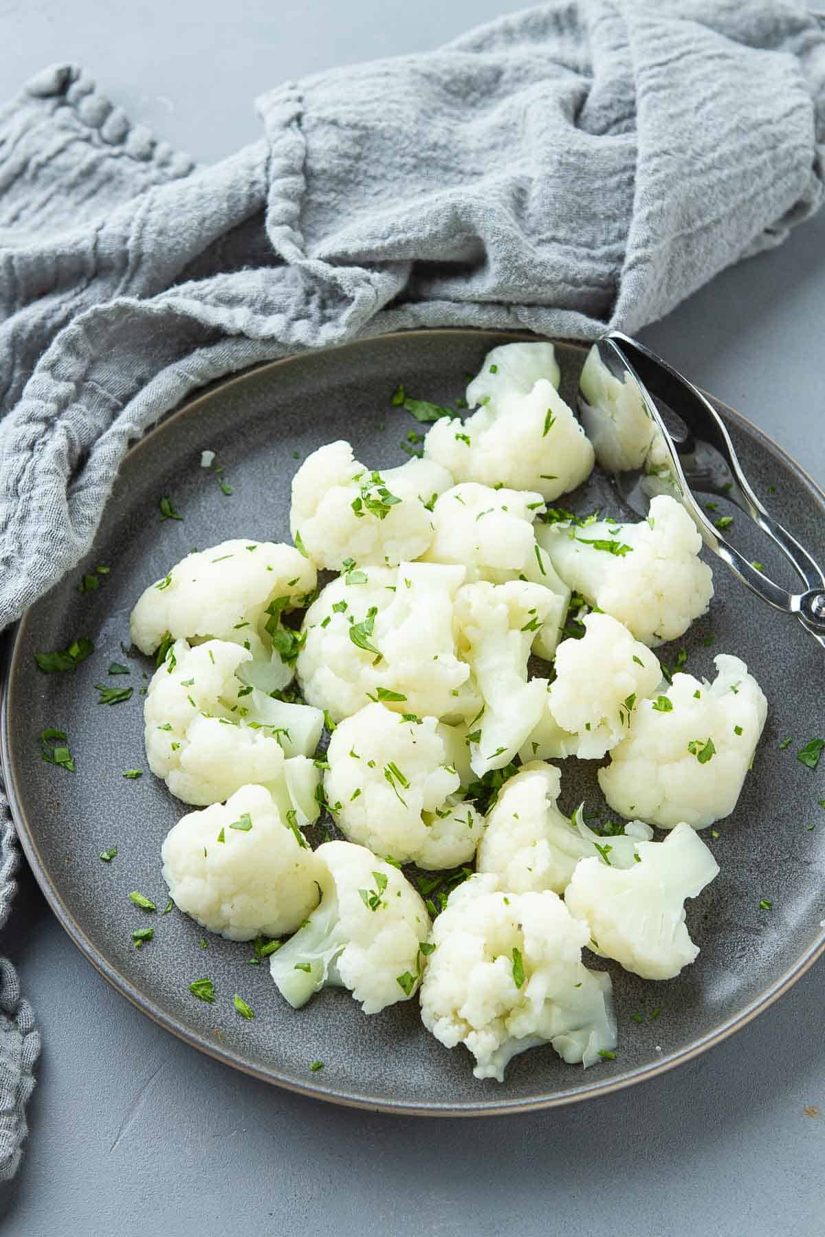 Cooked cauliflower on a dark gray plate, with a napkin on the side.