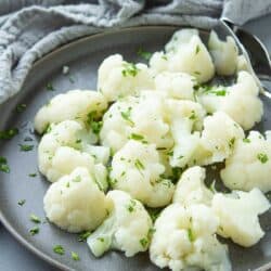 Steam cauliflower on a gray plate, garnished with parsley.