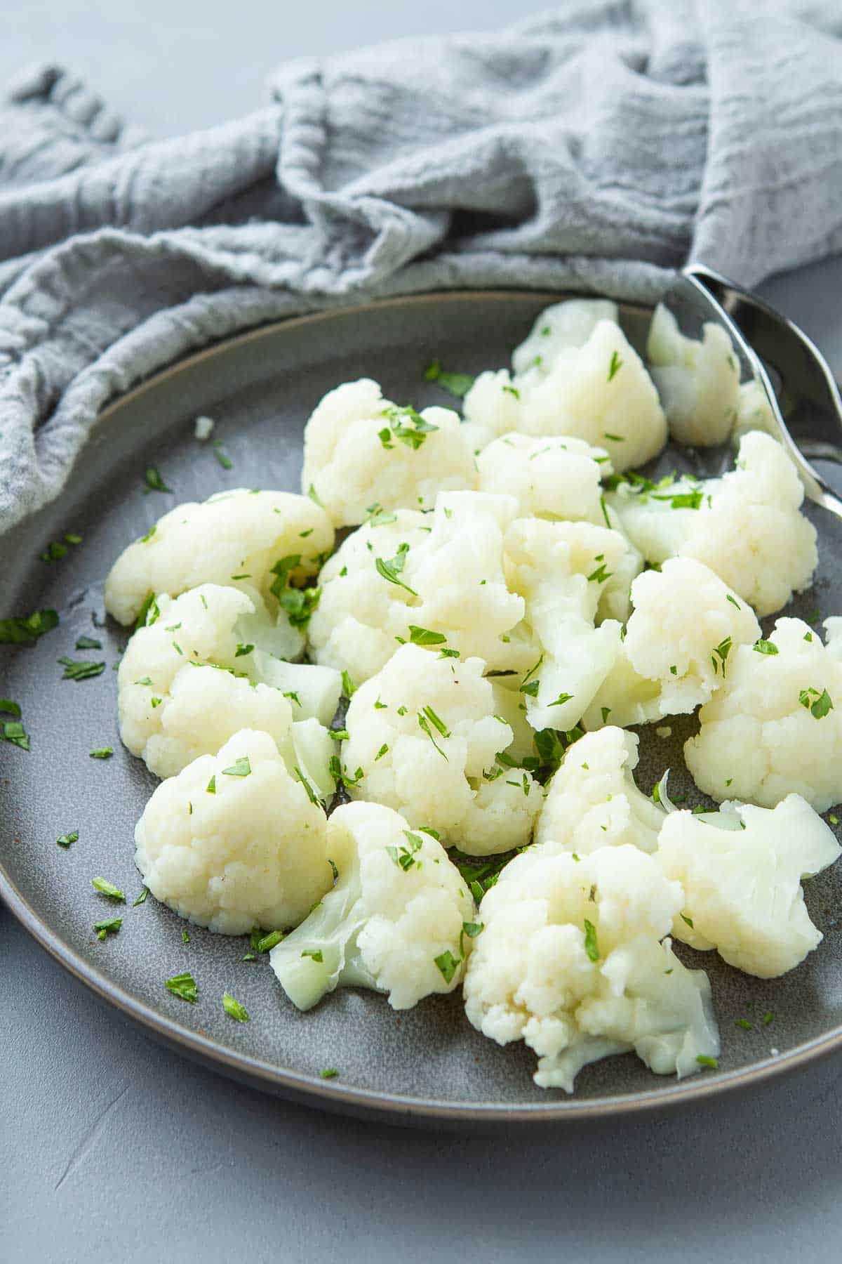 Steam cauliflower on a gray plate, garnished with parsley.