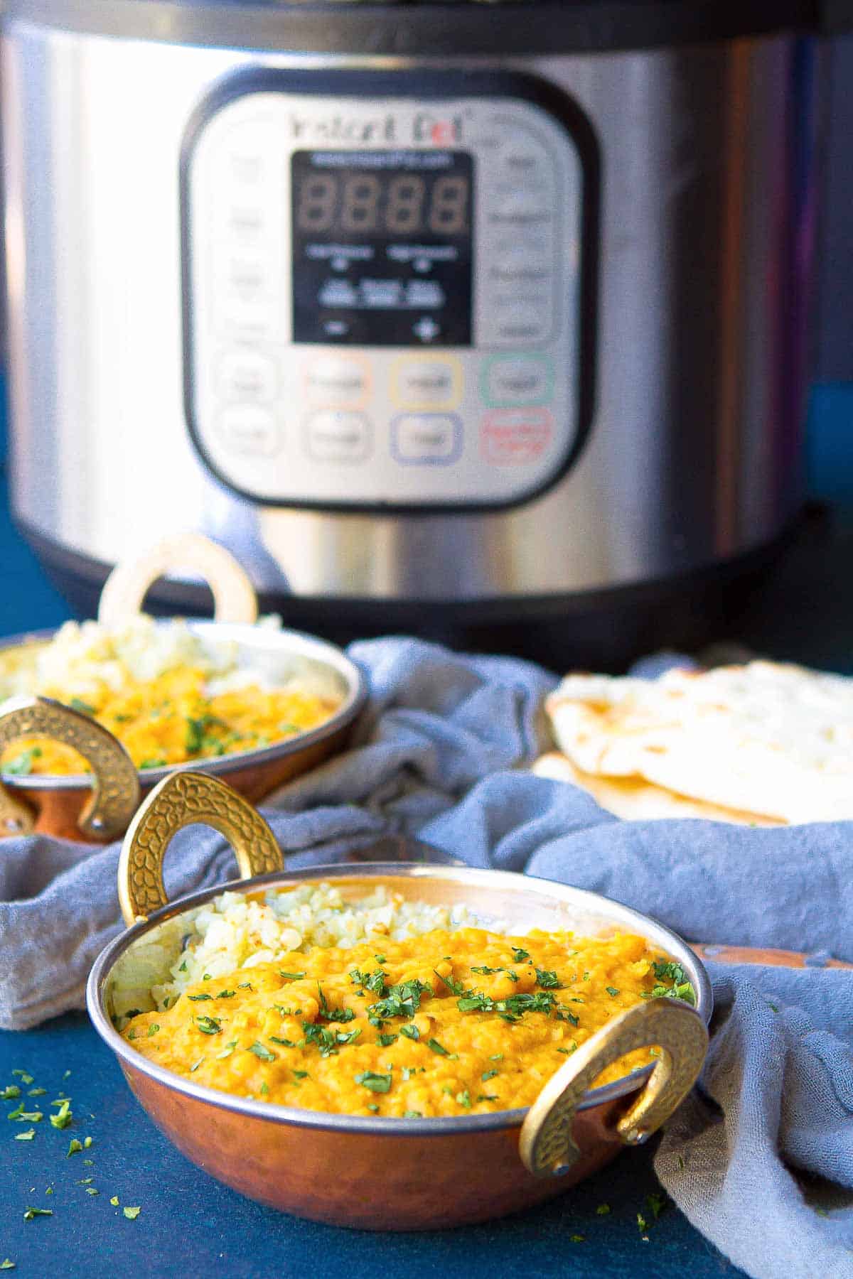 Red lentil dal in a brass bowl, with an Instant Pot in the background.