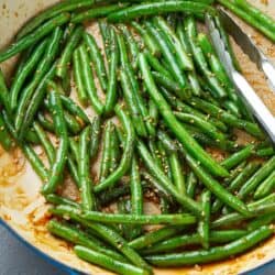 Stir-fried glazed green beans in a large ceramic skillet, with tongs.