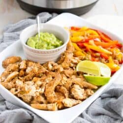 Cooked chicken, peppers and guacamole on a white platter.