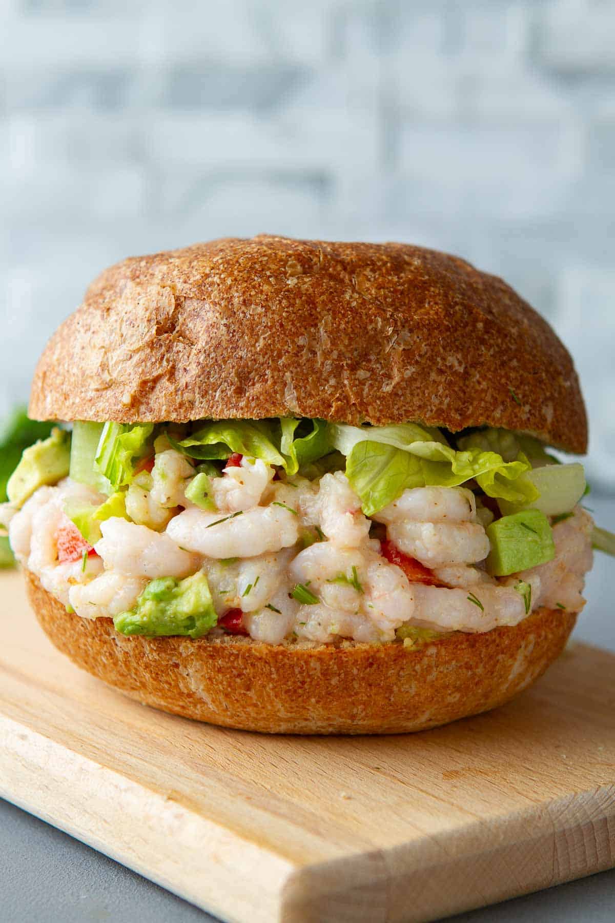 Shrimp salad sandwich with lettuce on a cutting board.