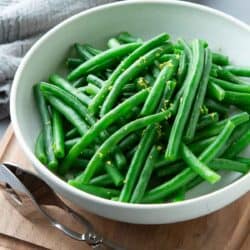 Steamed green beans in a white bowl, with tongs on the side.