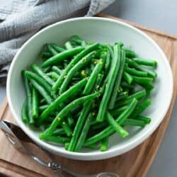 Steamed green beans with lemon zest in a white bowl.