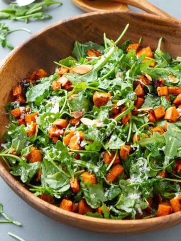 A wooden salad bowl filled with a sweet potato arugula salad.