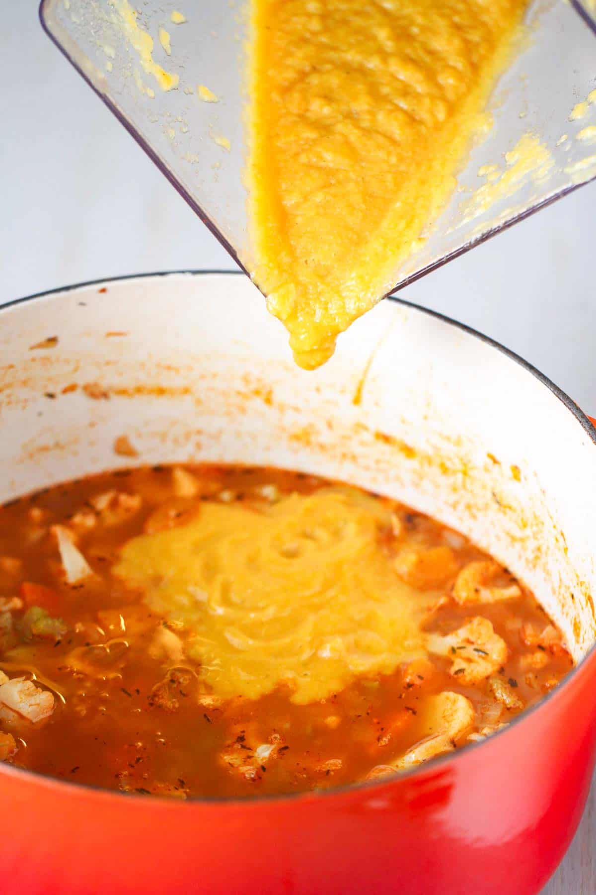 Pouring blended vegetable soup into a saucepan of broth and vegetables.