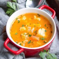 A thick vegetable soup with squash and cauliflower in a small red bowl.