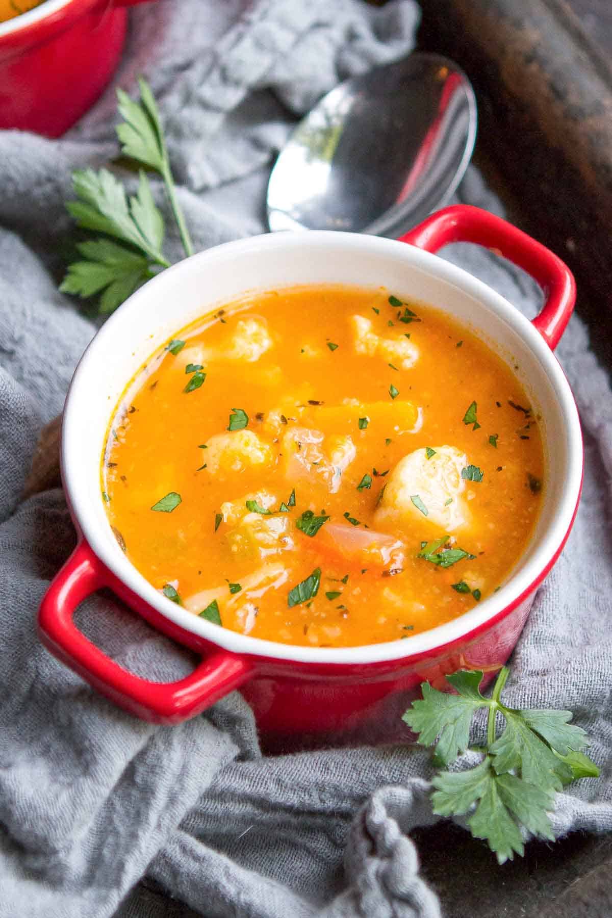 A thick vegetable soup with squash and cauliflower in a small red bowl.