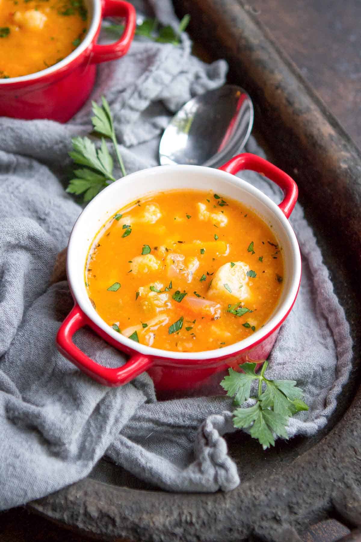 A red bowl full of butternut squash vegetable soup, resting on a metal tray.