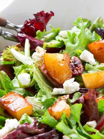 Glazed pears, greens, pecan and goat cheese in a white bowl.