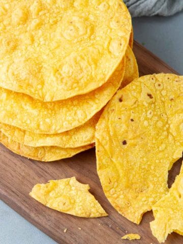 A stack of tostada shells, one broken, on a cutting board.