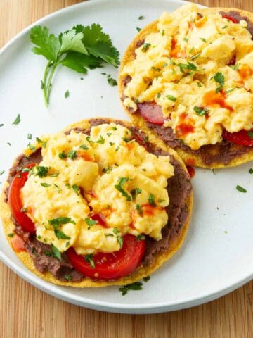 Two breakfast tostadas, topped with scrambled eggs, on a white plate.