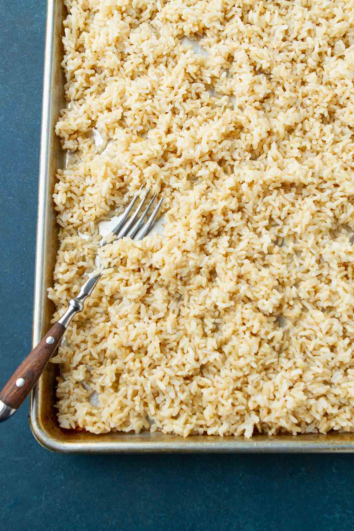 Cooked brown rice and a fork on a baking sheet.