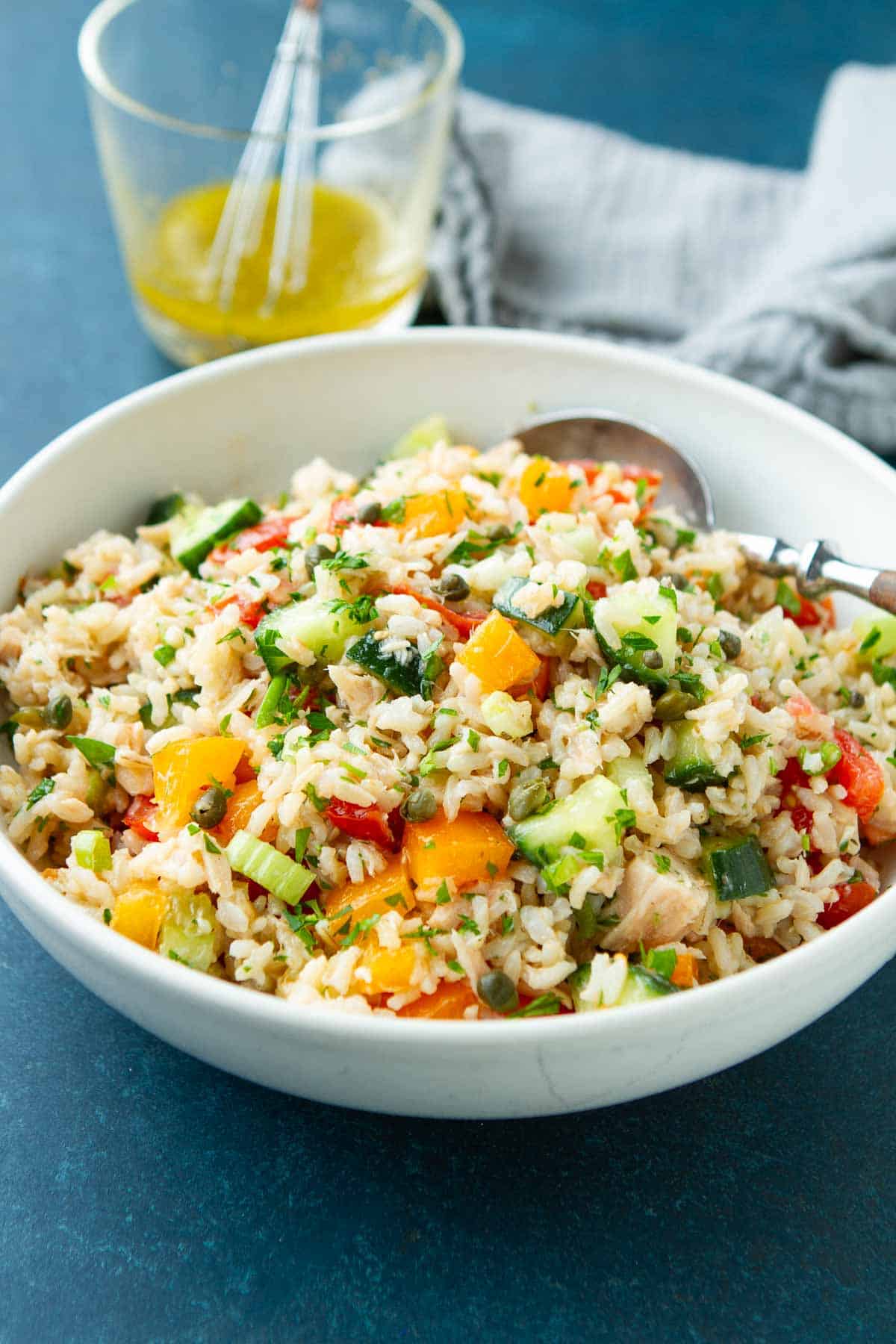 Tuna rice salad with vegetables in a white bowl, plus a glass container with dressing.