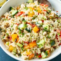 Rice salad with tuna, vegetables and spoon in a white bowl.