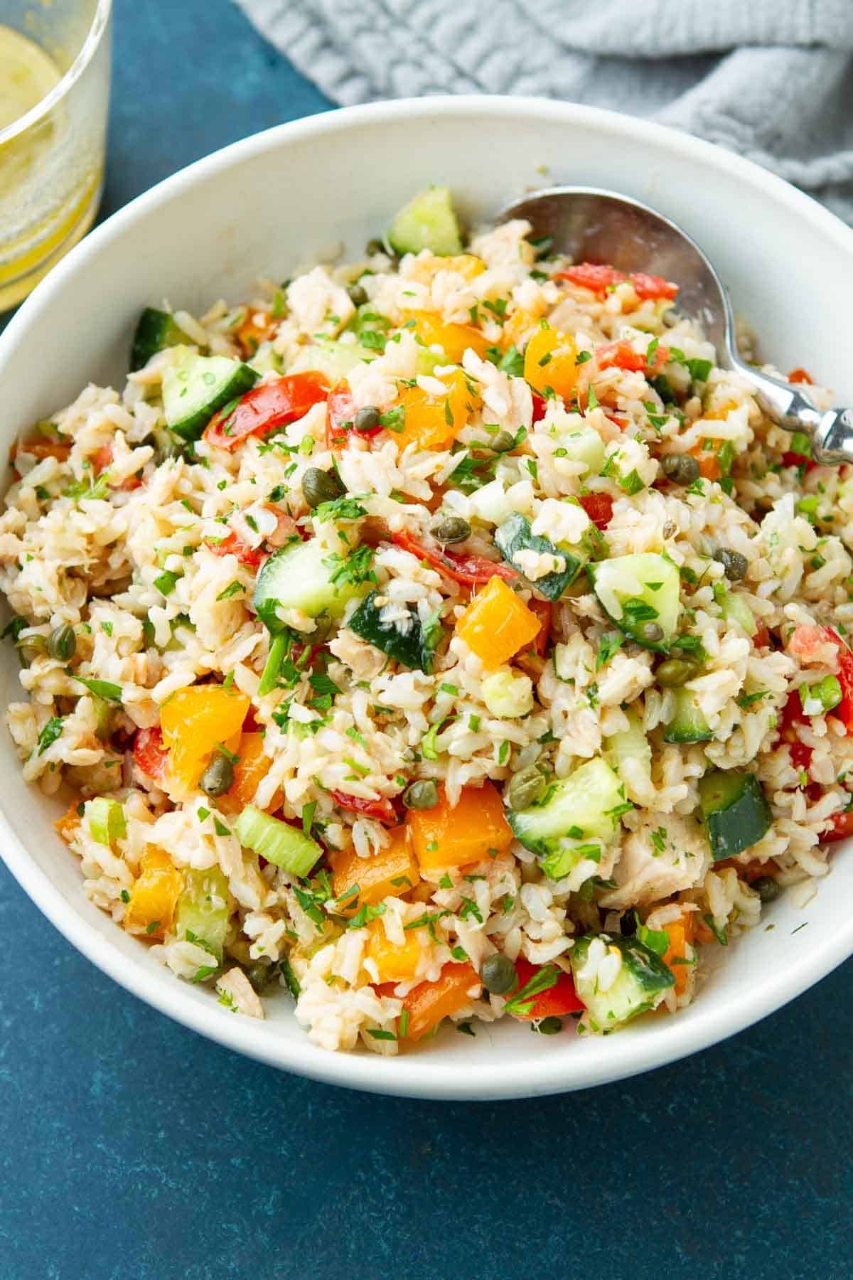 Rice salad with tuna, vegetables and spoon in a white bowl.