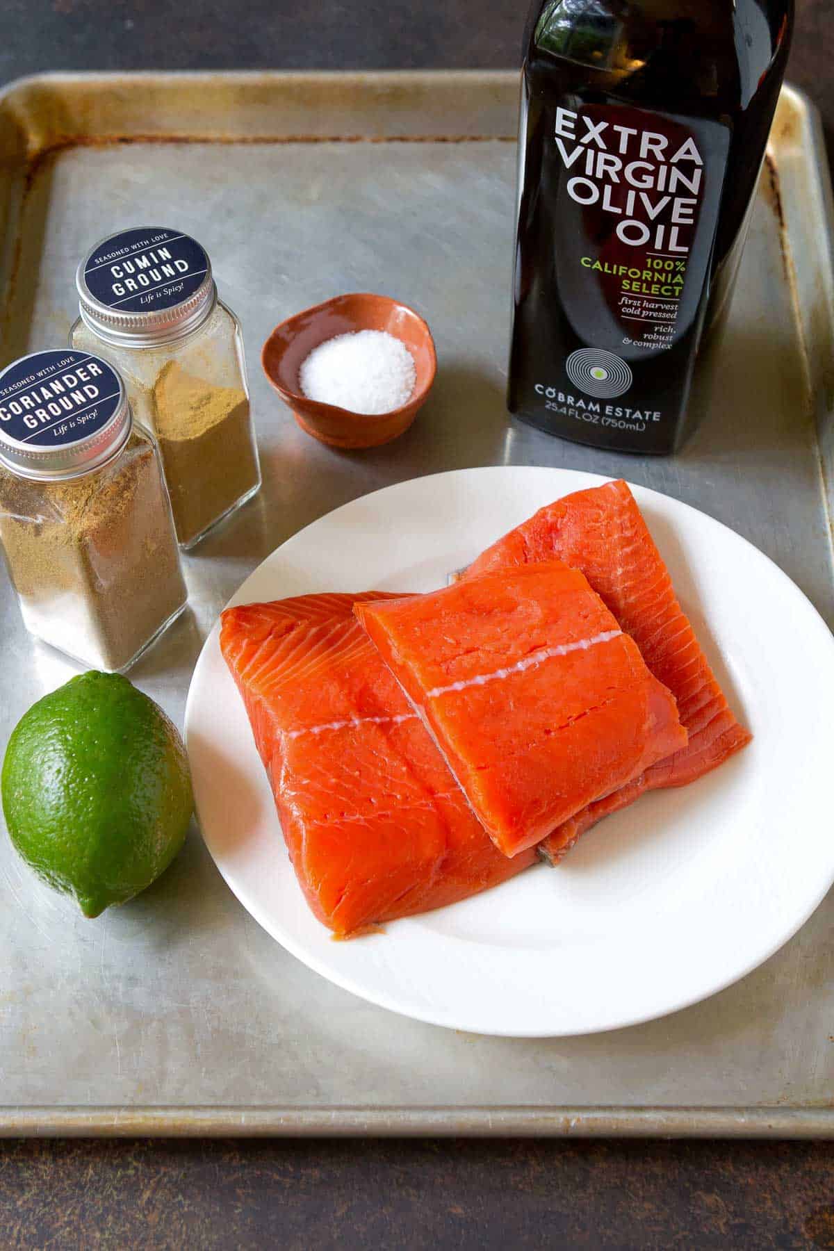 Raw salmon filets, spices, lime and olive oil on a baking sheet.