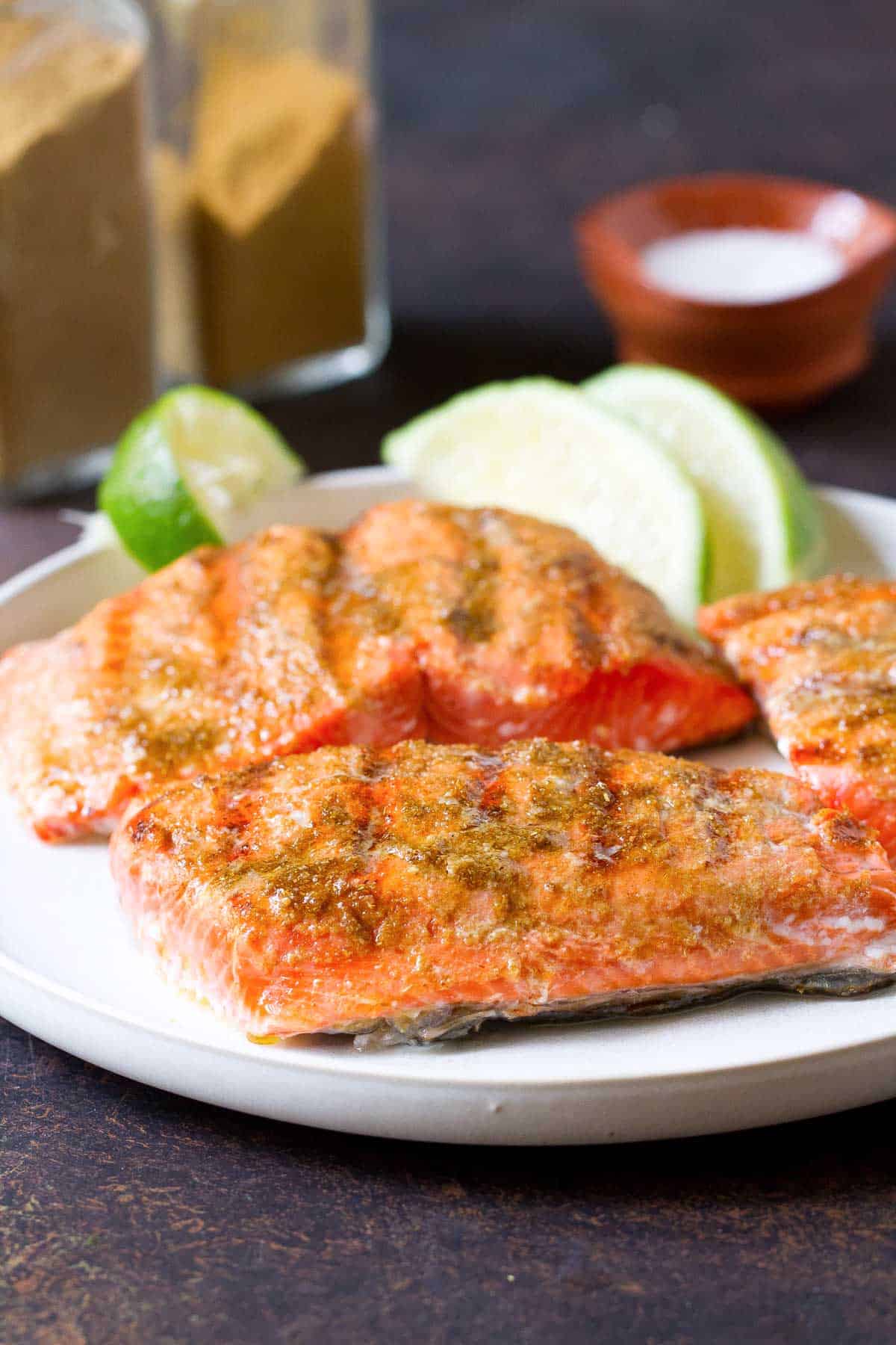 Pieces of grilled salmon and lime wedges on a white plate.