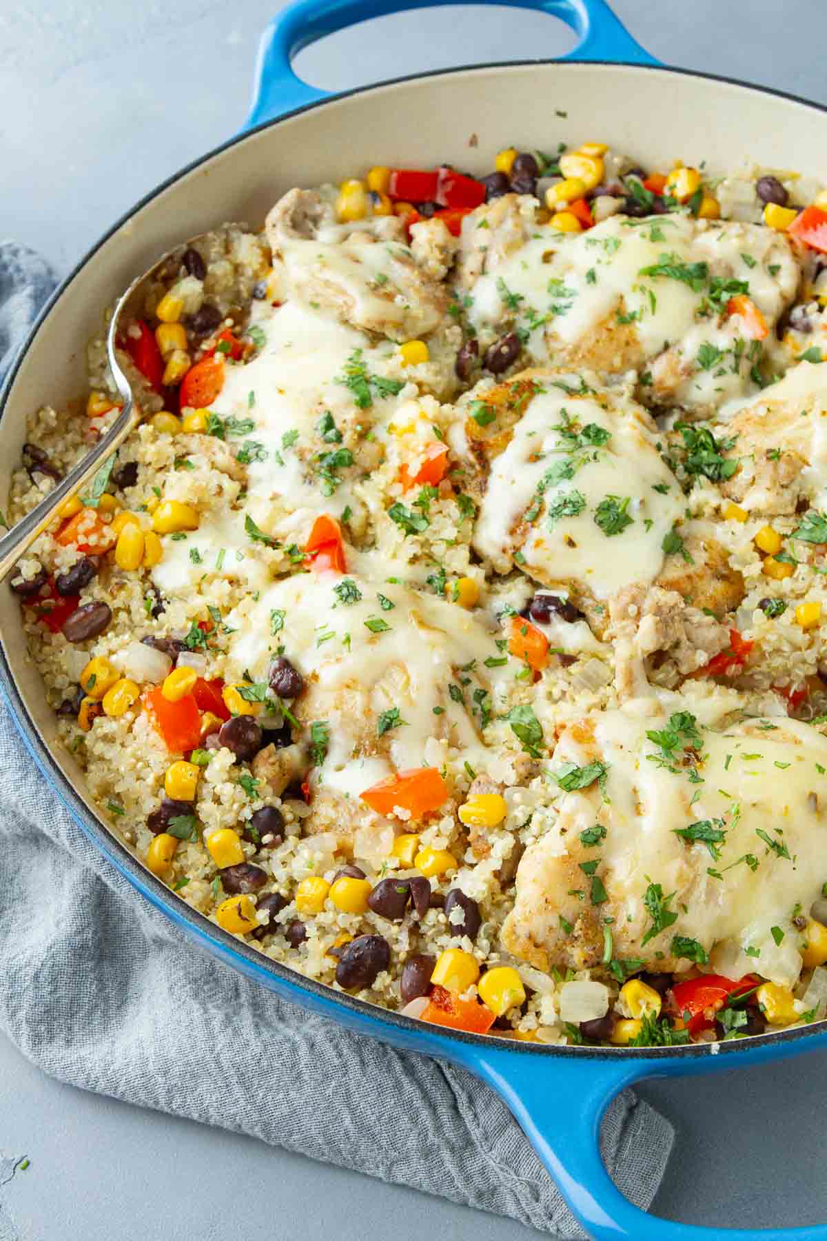 A large blue skillet filled with chicken, melted cheese, quinoa and vegetables.