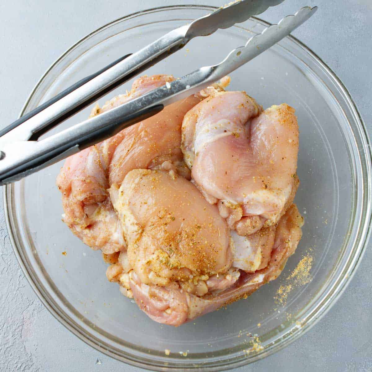 Seasoned raw chicken thighs in a glass bowl.