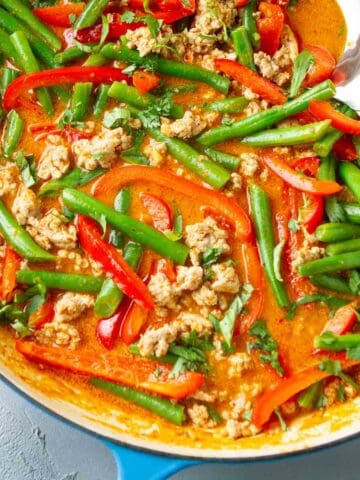 Red curry with ground turkey and vegetables in a blue and white skillet.