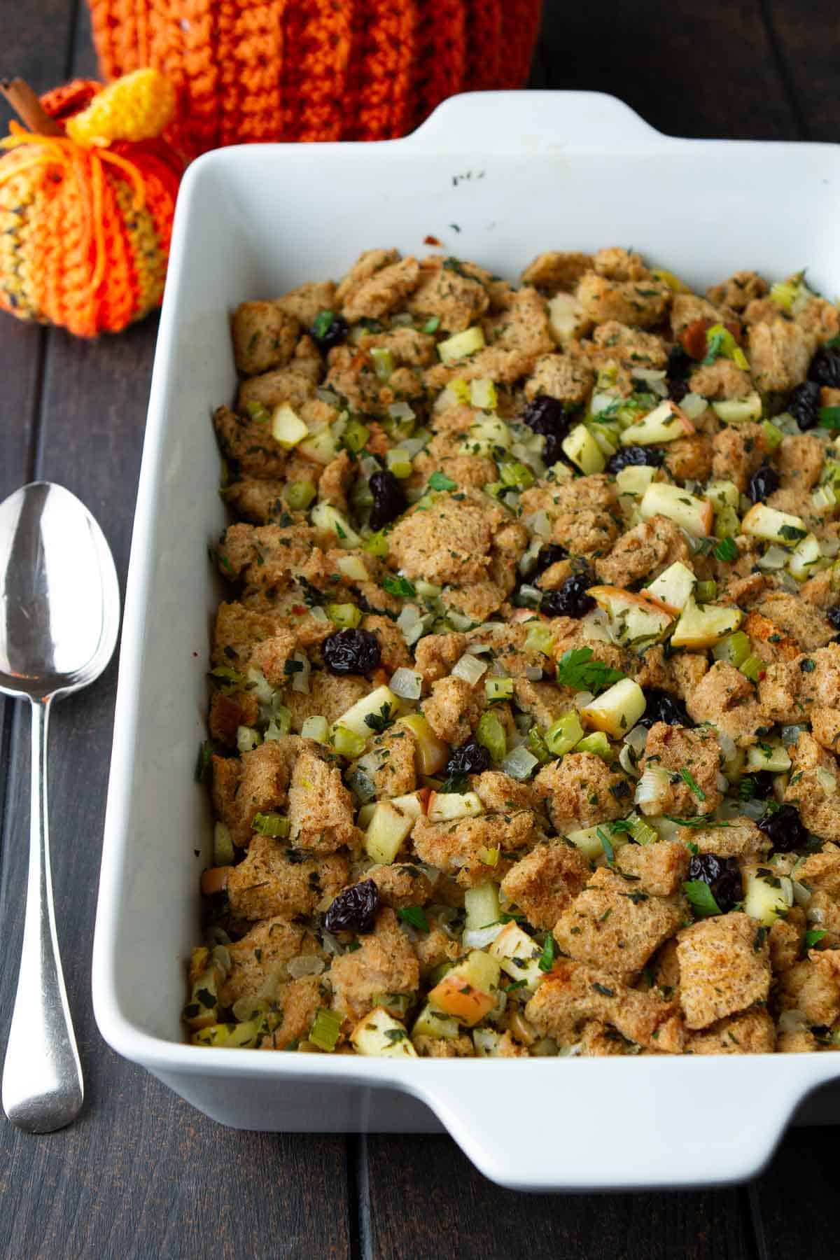 Bread stuffing with apples and cherries in a white baking dish.