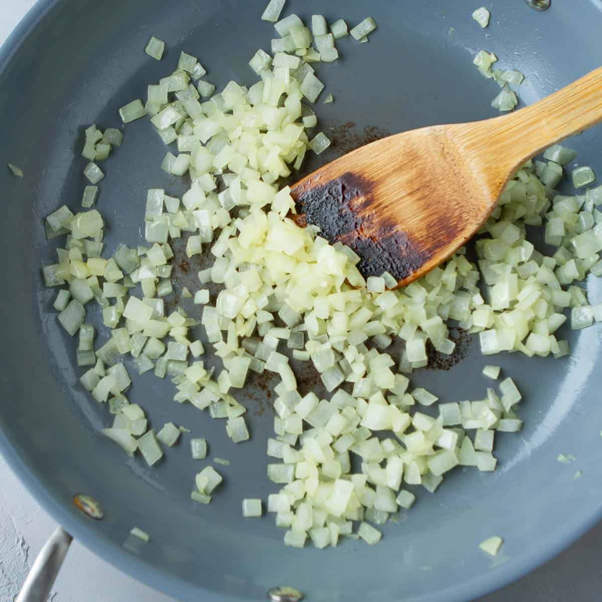 Cooked chopped onions and a wooden spatula in a large skillet.