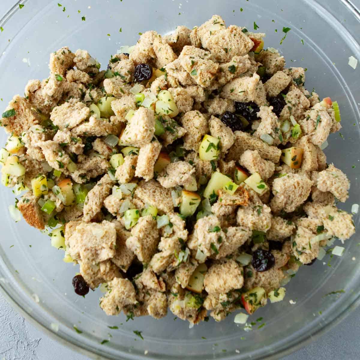 Bread cubes mixed with cooked vegetables and dried cherries in a glass bowl.