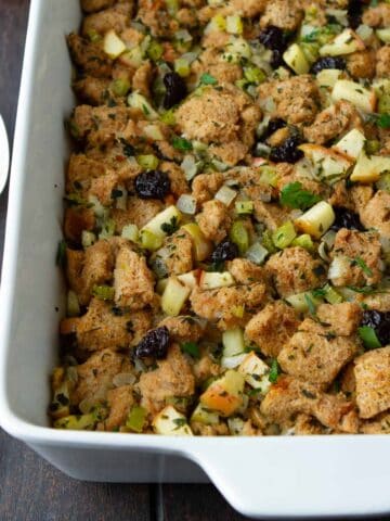 Bread stuffing with apples and cherries in a white baking dish.