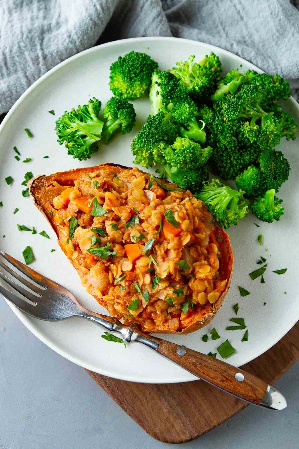 Lentil stuffed sweet potato and broccoli on a white plate.